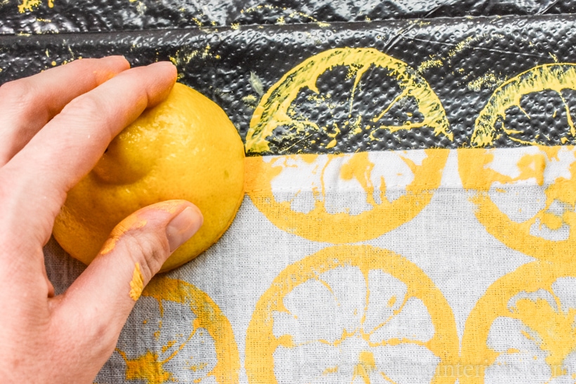 close-up of hand stamping a lemon on a white four sack towel to create a citrus print