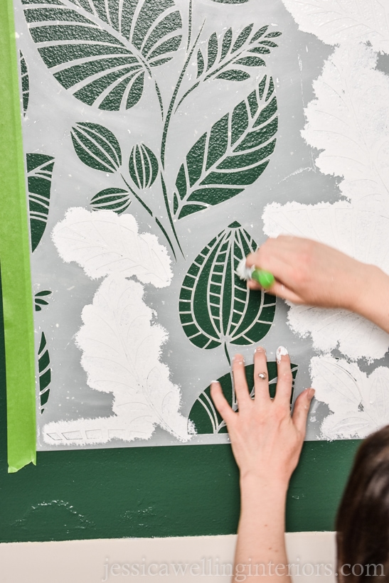 woman using a stencil brush to apply white paint to a wall stencil 
