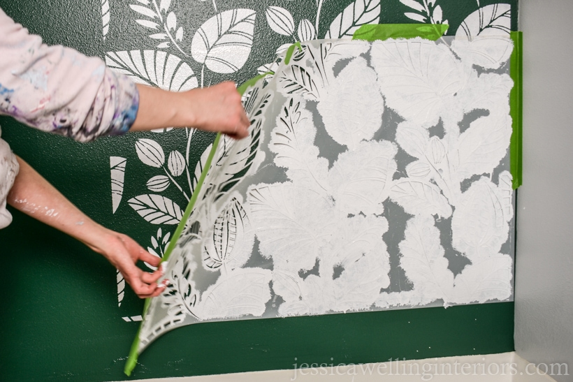 woman's hands pulling a large wall stencil away from the wall to reveal the stenciled pattern underneath