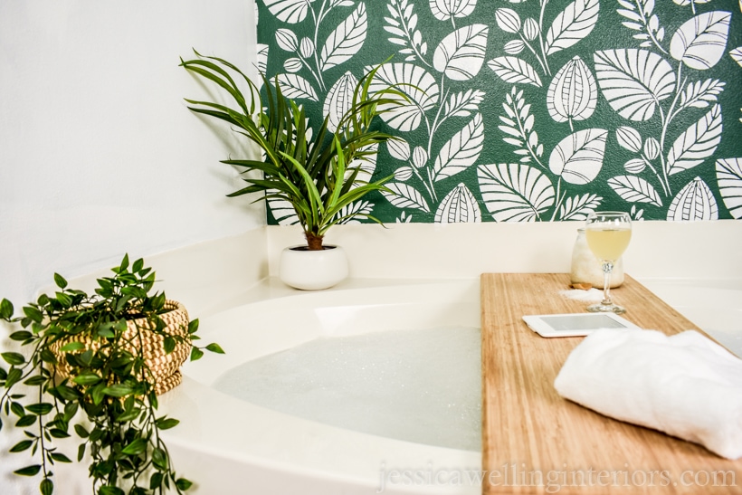 bathtub with a bath tray and plants in front of a finished stenciled wall