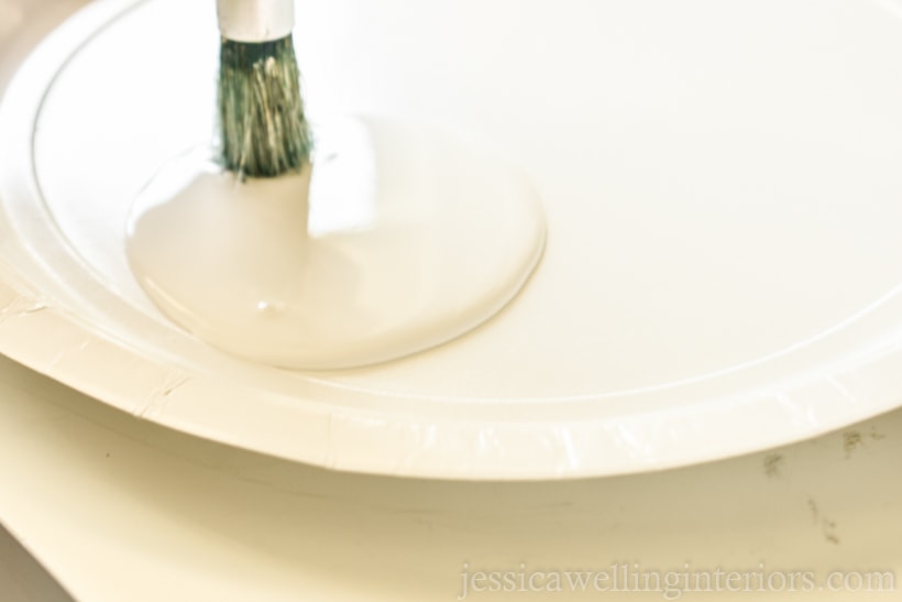 close-up of a white paper plate with a stencil brush dipping into a puddle of white paint