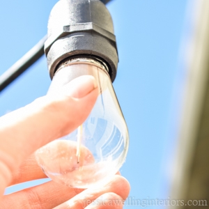 close-up of a string light bulb hanging with a hand twisting it into place