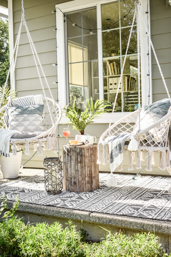 2 Boho porch swings with sring lights, an outdoor rug, and an end table