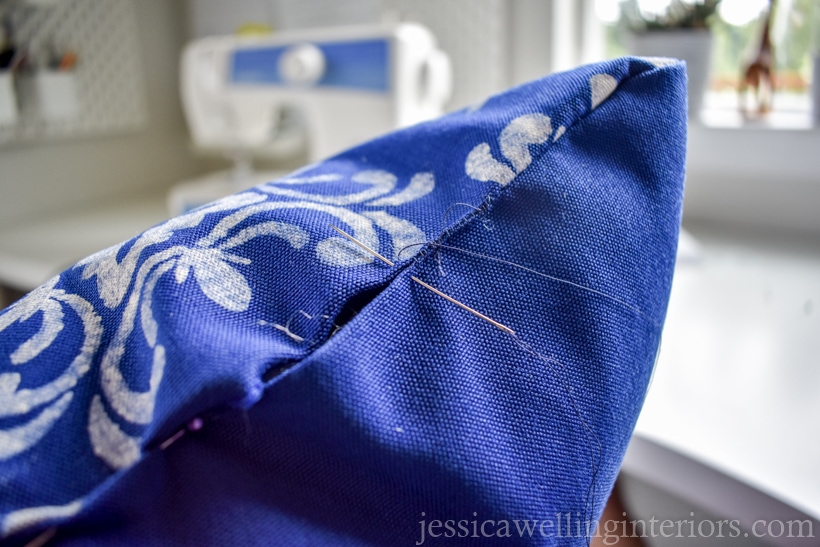 close-up of a hand-sewing needle sewing the opening closed on an outdoor pillow