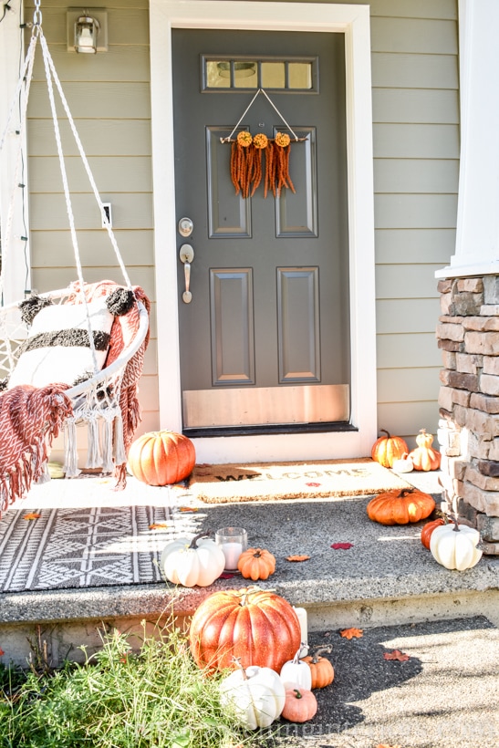 front door and porch decorated for Fall, with a modern Boho wreath and pumpkins