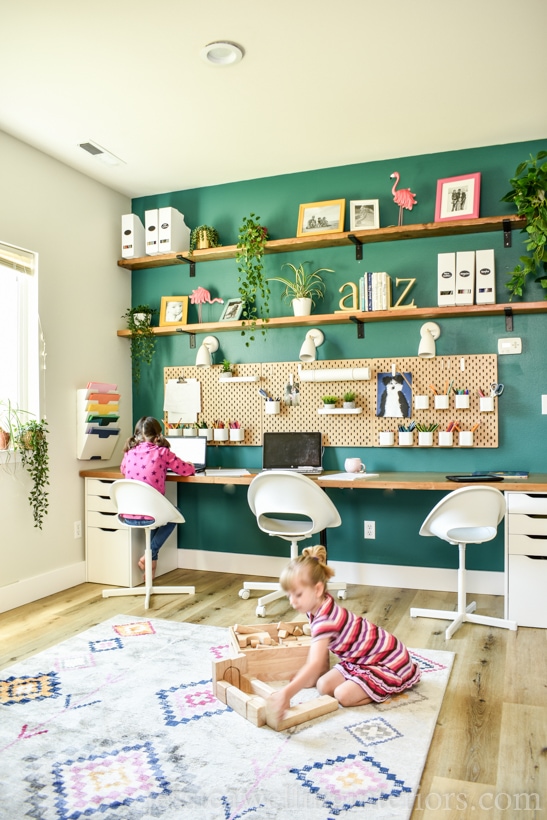 homeschool room with a long school desk for home with 3 work stations- 1 child working at the desk, and another playing with blocks on the floor