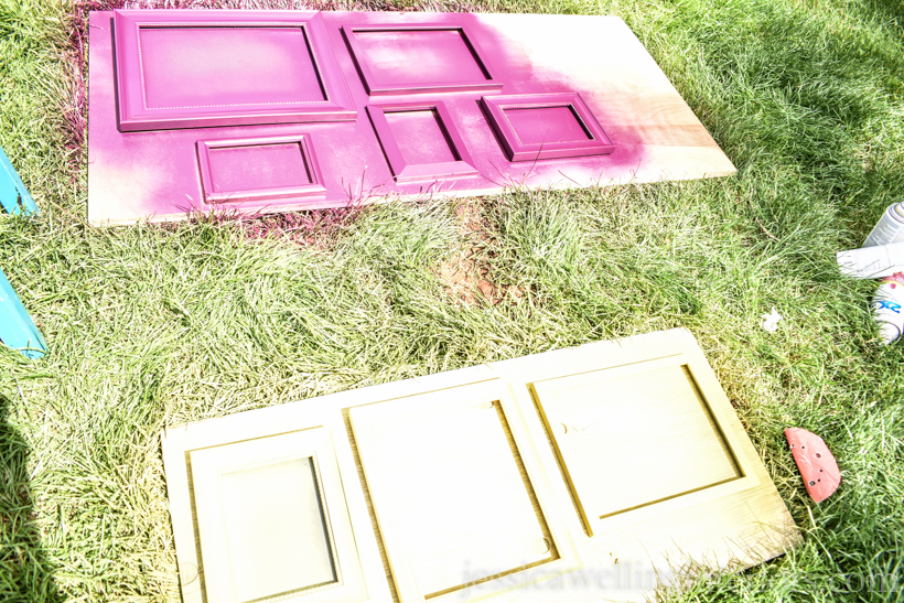 piece of plywood laying on grass, with several picture frames being spray painted purple and yellow