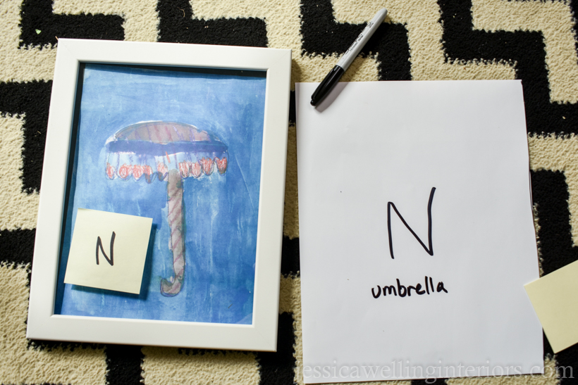 white frame with a child's watercolor painting and a cut-out of paper of the same size, both with the letter "N"