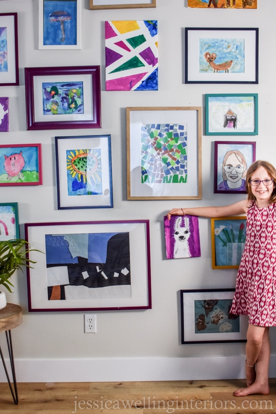 finished kids art display wall with a little girl pointing to a llama painting