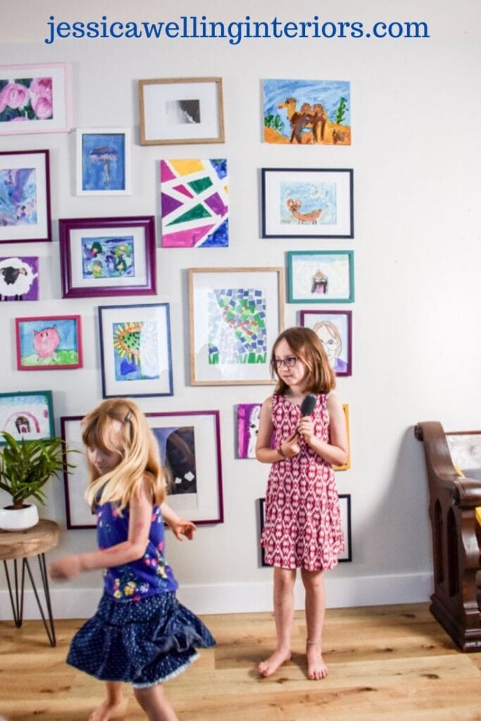 kids' art gallery wall with two little girls singing and dancing in front of it