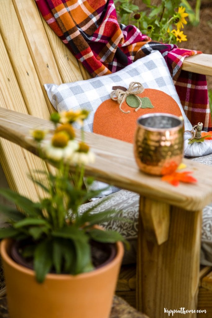 adirandack chair decorated for Fall with a DIY pumpkin pillow, plaid throw blanket, and a copper mug