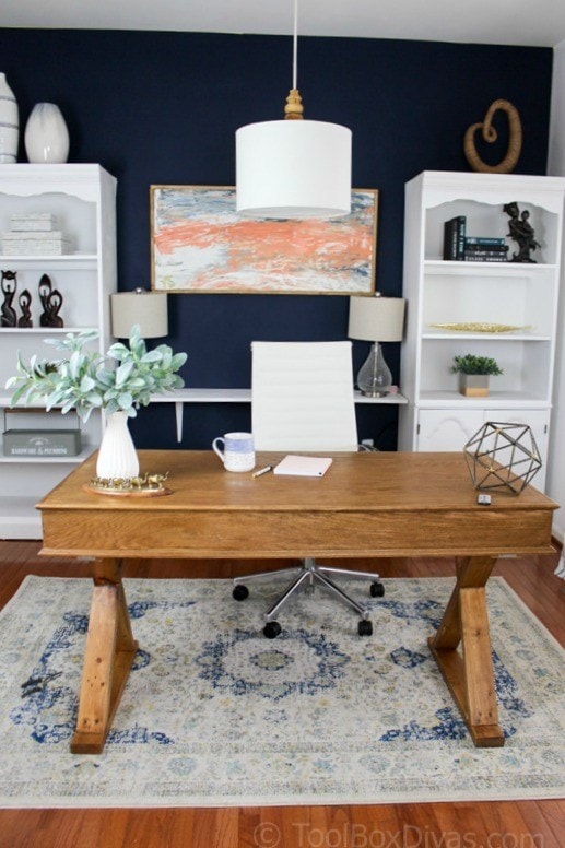 modern home office design with a large wood desk in the center of the room, and bookcases and a painting as a Zoom backdrop