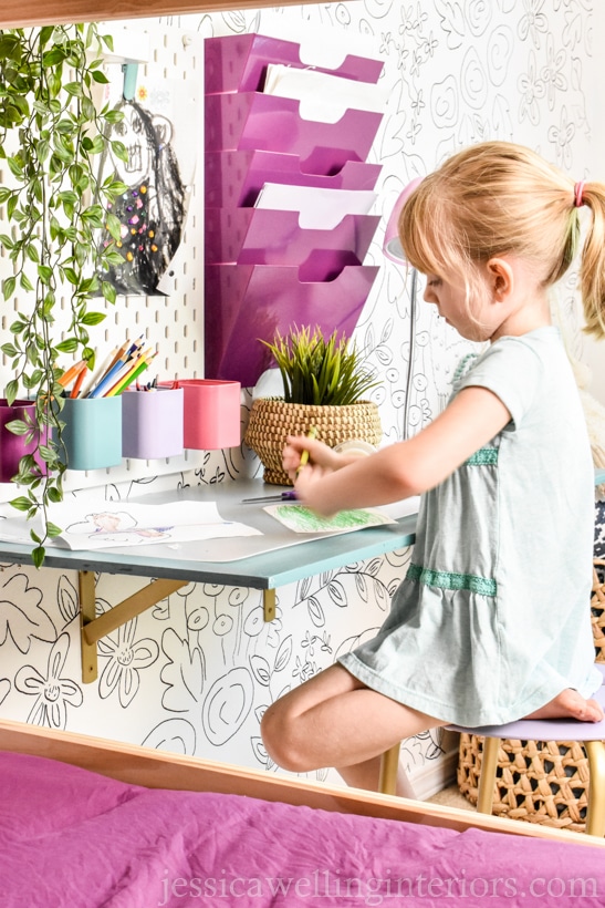 child working at a small DIY floating desk made using plywood and metal brackets, with Ikea Skadis pegboard and Kvissle file storage on the wall