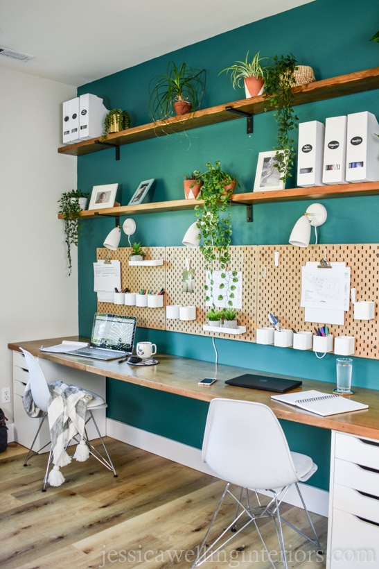 long Ikea Alex desk with two Alex drawer units, Skadis pegboard storage, floating shelves, and indoor plants against a dark green accent wall