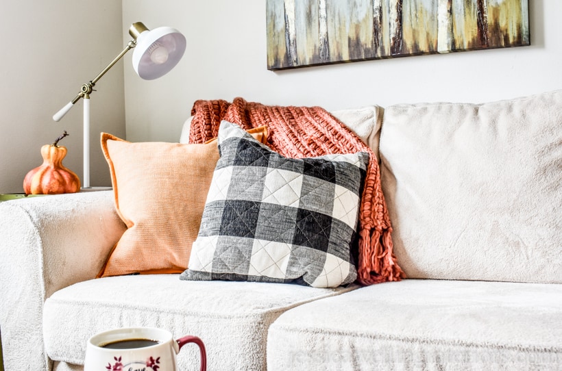 Fall throw pillows and an orange throw blanket on a sofa