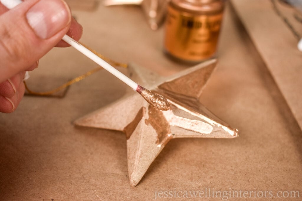 hand using a que tip to apply gold leaf paint to a DIY Christmas ornament