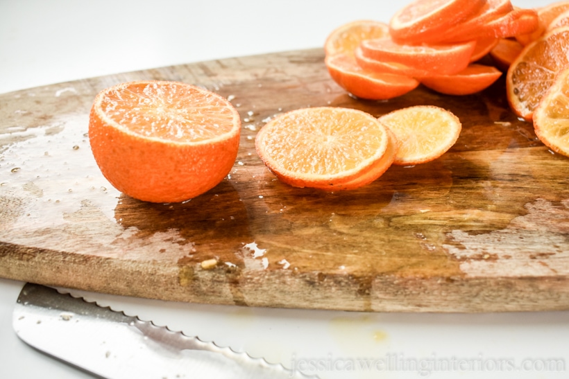 cutting board with a serrated knife and an orange being cut into slices