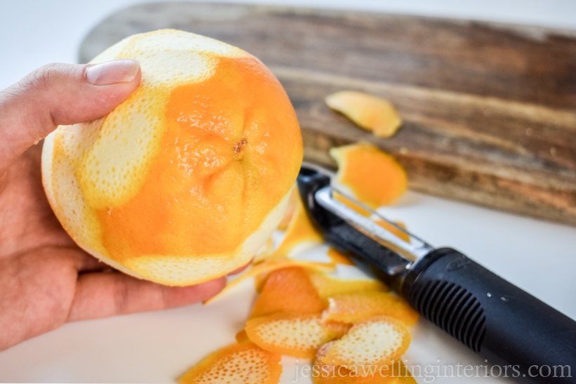 close-up of orange partially peeled with a potato peeler in the background