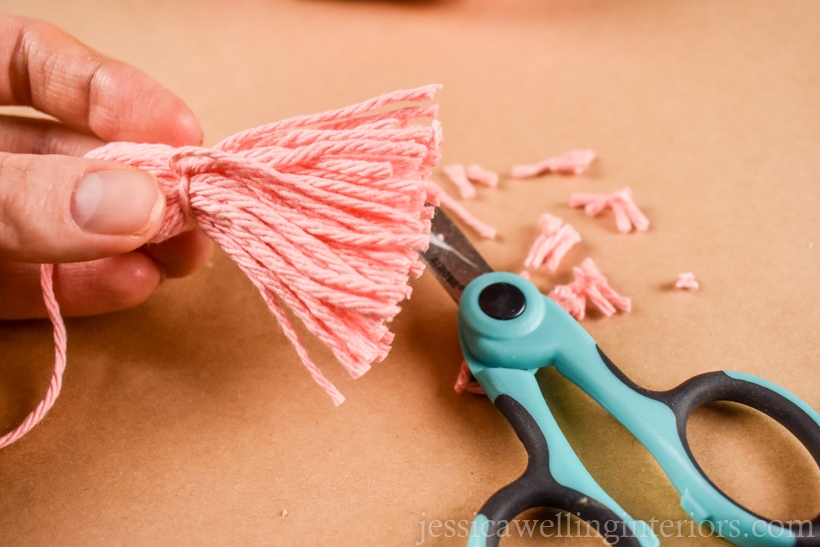 hand holding a small yarn tassel after the ends of yarn have been trimmed with scissors