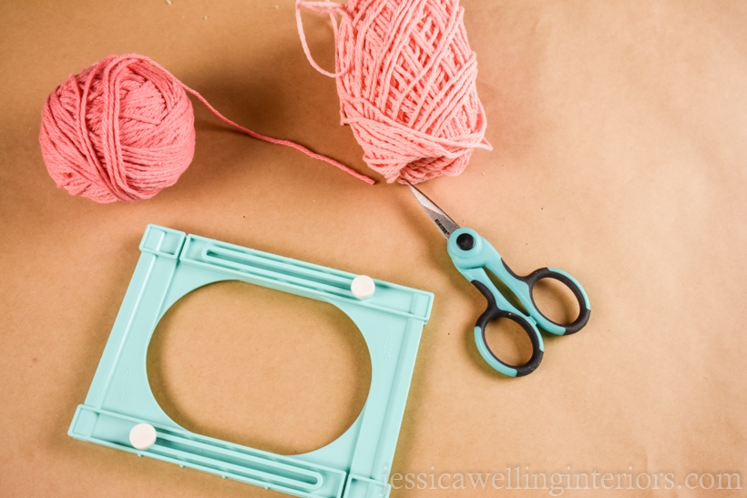 yarn tassel supplies on a table- a Clover tassel maker, 2 balls of yarn, and a pair of sharp craft scissors