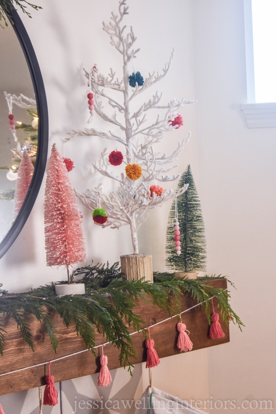 mantel decorated for Christmas with a Boho tassel garland, trees with colorful pom poms, etc.