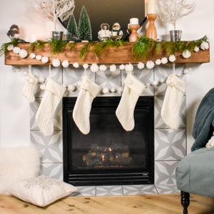 mantel decorated for Christmas with a pom pom garland and Christmas stockings