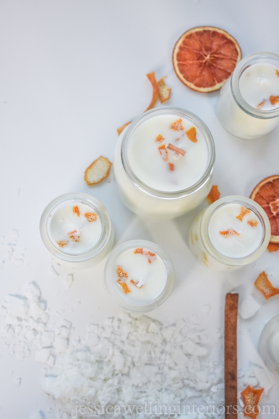 flat lay image of several siy soy candles with bits of orange peel, cinnamon sticks, dried orange slices, and soy wax flakes