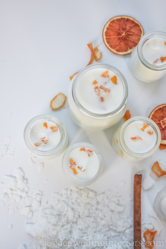 how to make soy candles: several orange scented candles with orange peel, cinnamon sticks, and soy wax flakes