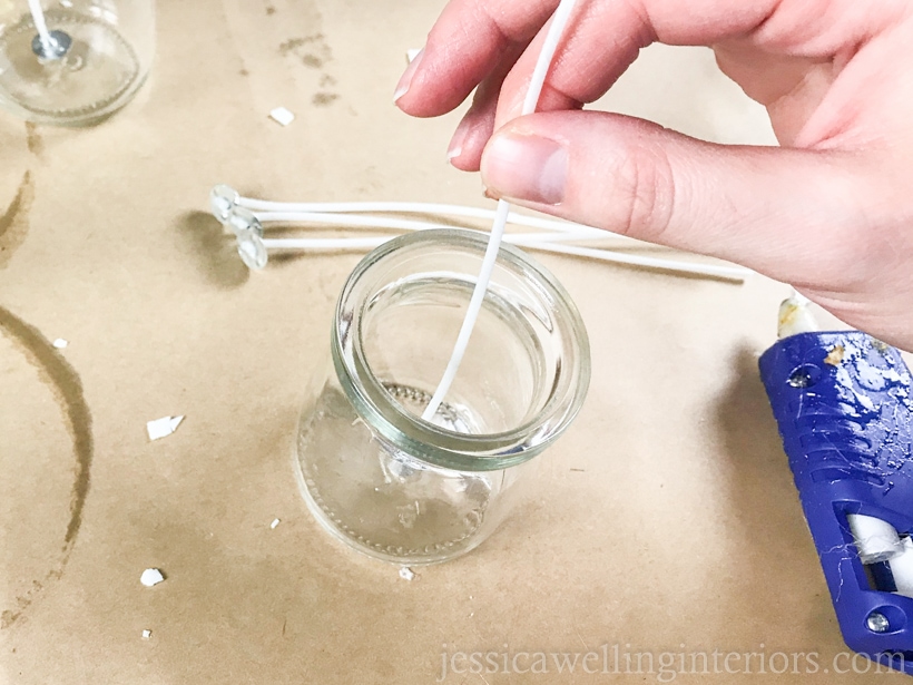 hand attaching cotton candle wick to the bottom of a glass candle jar to make a soy candle