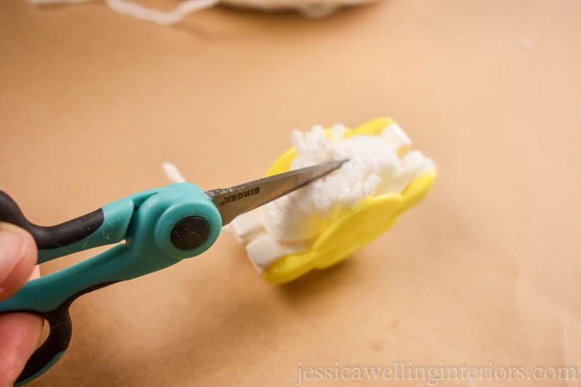 close-up of scissors cutting the yarn on a pom pm maker to make a pom pom garland