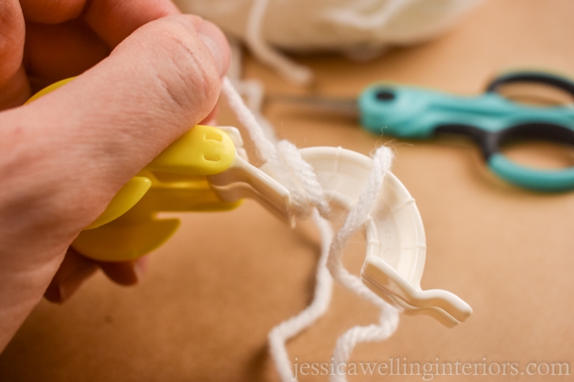 close-up of hand wrapping white yard around a small pom pom maker