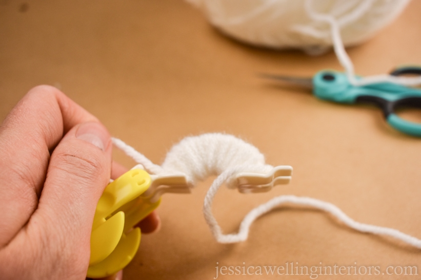 close-up of a hand holding a small pom pom maker with white yarn wrapped around one side