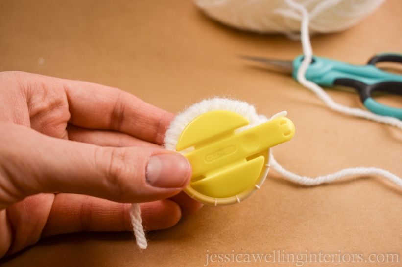 hand holding a small yellow pom pom maker with white yarn wrapped around one side