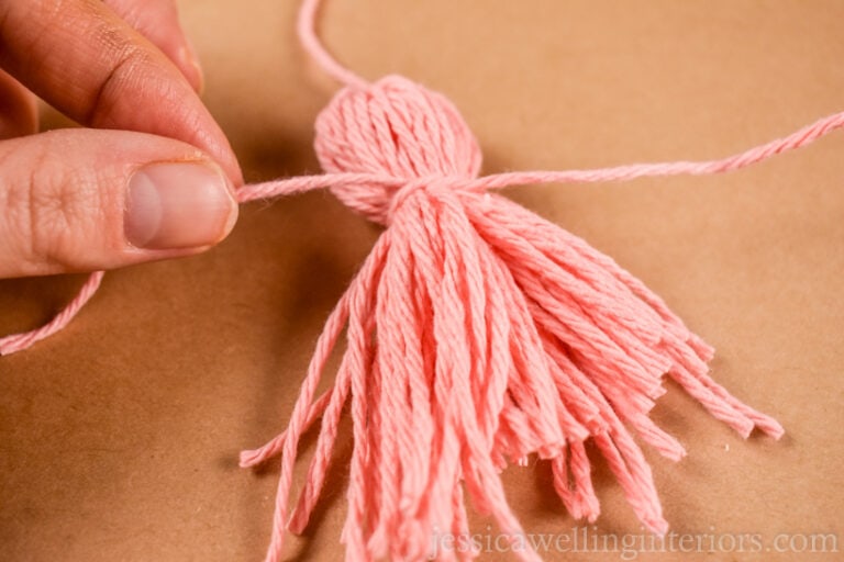 fingers tying a pink yarn tassel onto a DIY tassel garland