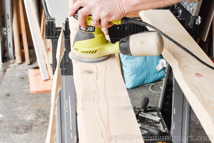 hand using an orbital sander to sand a wood coat rack before applying wood stain