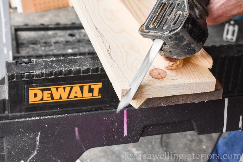 close-up of a reciprocating saw cutting an uneven, angled line across the top of a diy coat rack