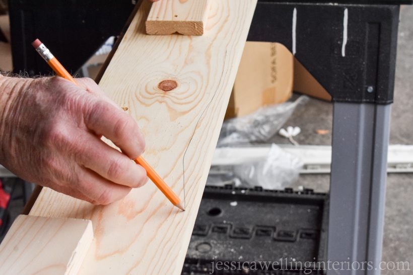 close-up of a hand using a pencil to draw an uneven line across the top of a board to make a faux live edge