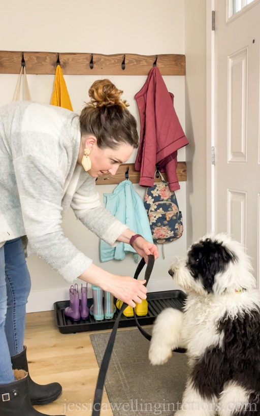 woman putting leash on a sheepadoodle puppy in a modern entryway with DIY wall hook racks behind her