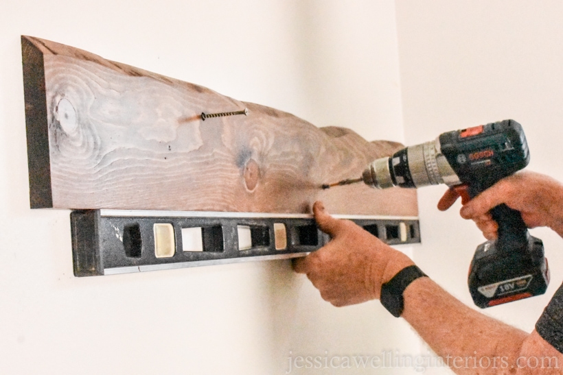 diy coat rack with a faux live edge being mounted to the entryway wall with wood screws