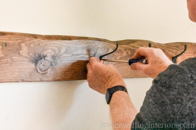 black metal wall hooks being attached to a wall-mounted coat rack