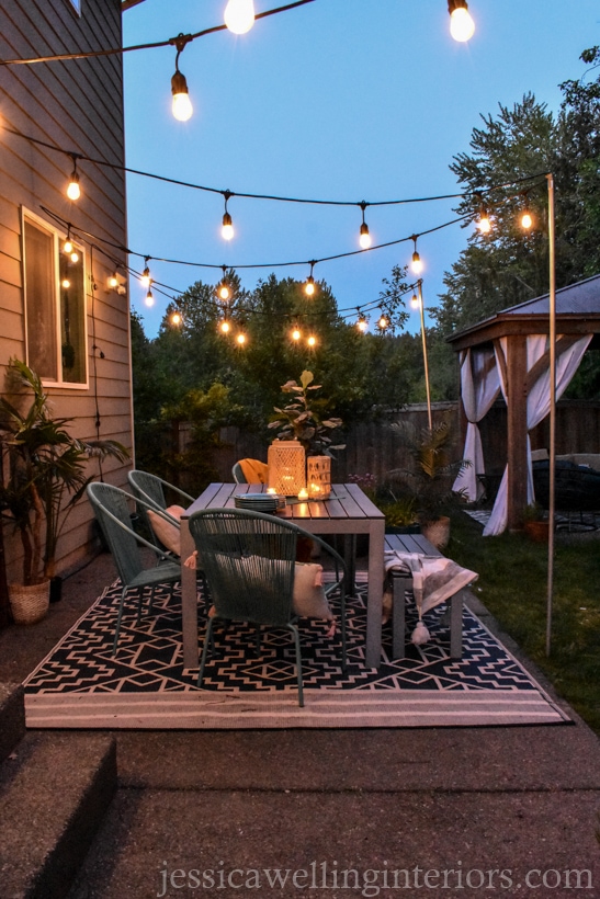 modern patio with glowing string lights, a Boho outdoor rug in black & white, and an outdoor dining table