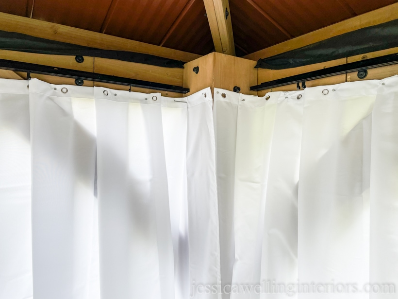 two outdoor curtain panels hung in the corner of a wood Costco gazebo