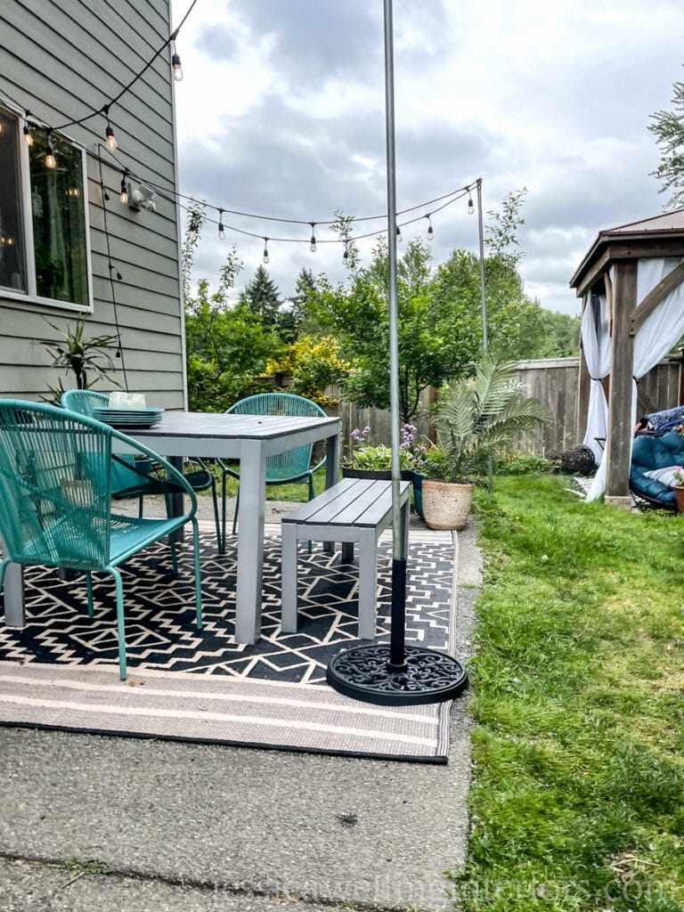 backyard patio with simple DIY outdoor string light poles made from umbrella bases and electrical conduit