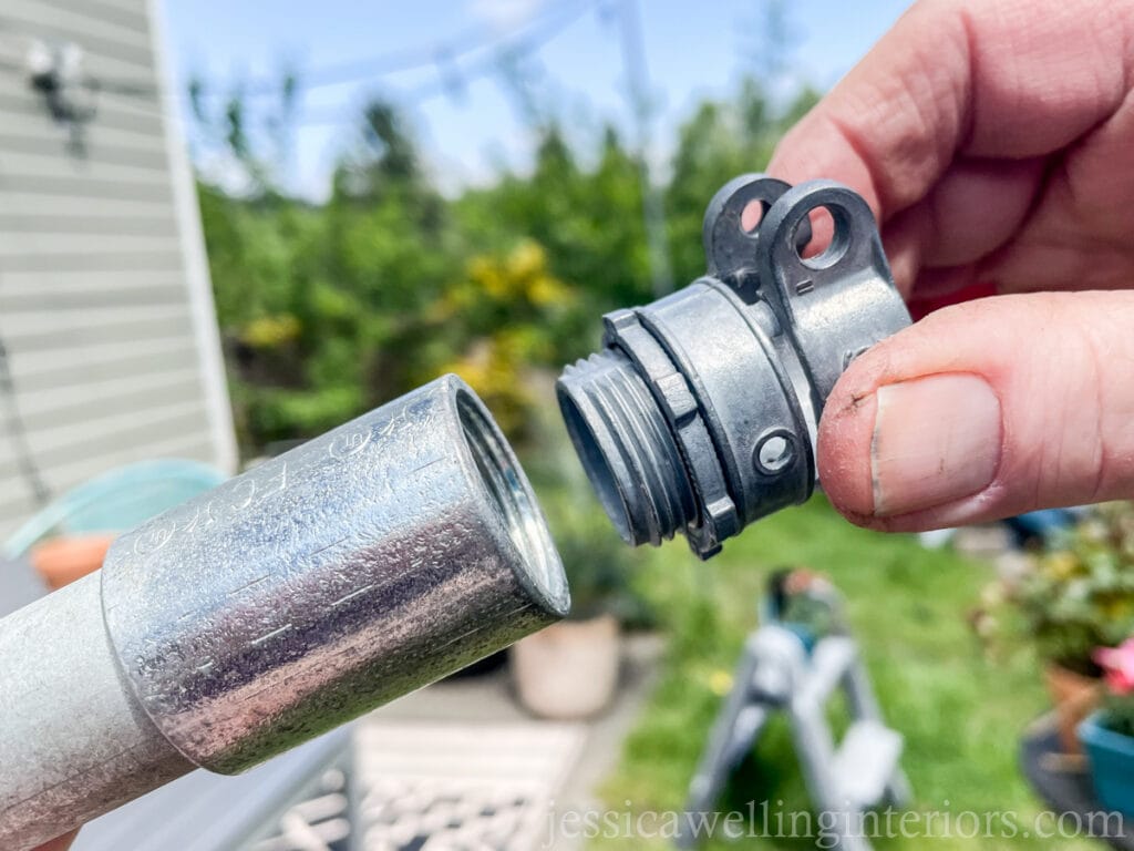 close-up of a hand screwing a threaded coupling onto the end of an electrical conduit pipe to make a DIY string light pole