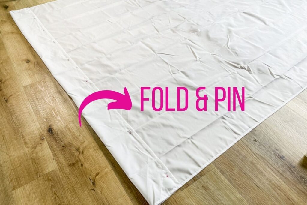 polyester shower curtain laid out on the floor with the hem folded and pinned with sewing pins