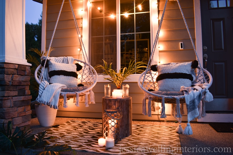 porch with glowing string lights draped over a window and two macrame swing chairs