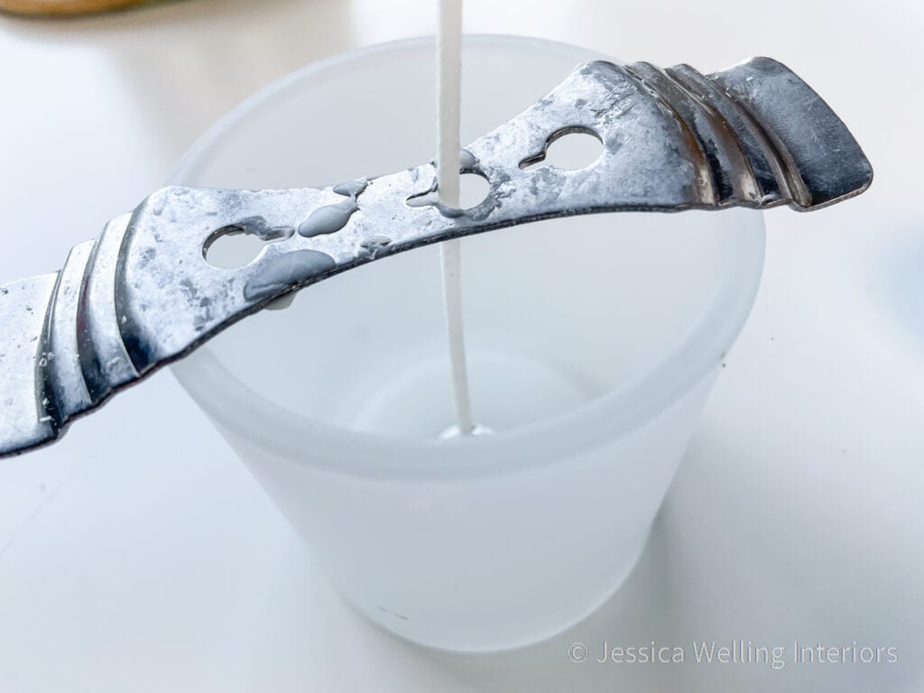 small glass container with a candle wick and wick holder, ready to be filled with wax