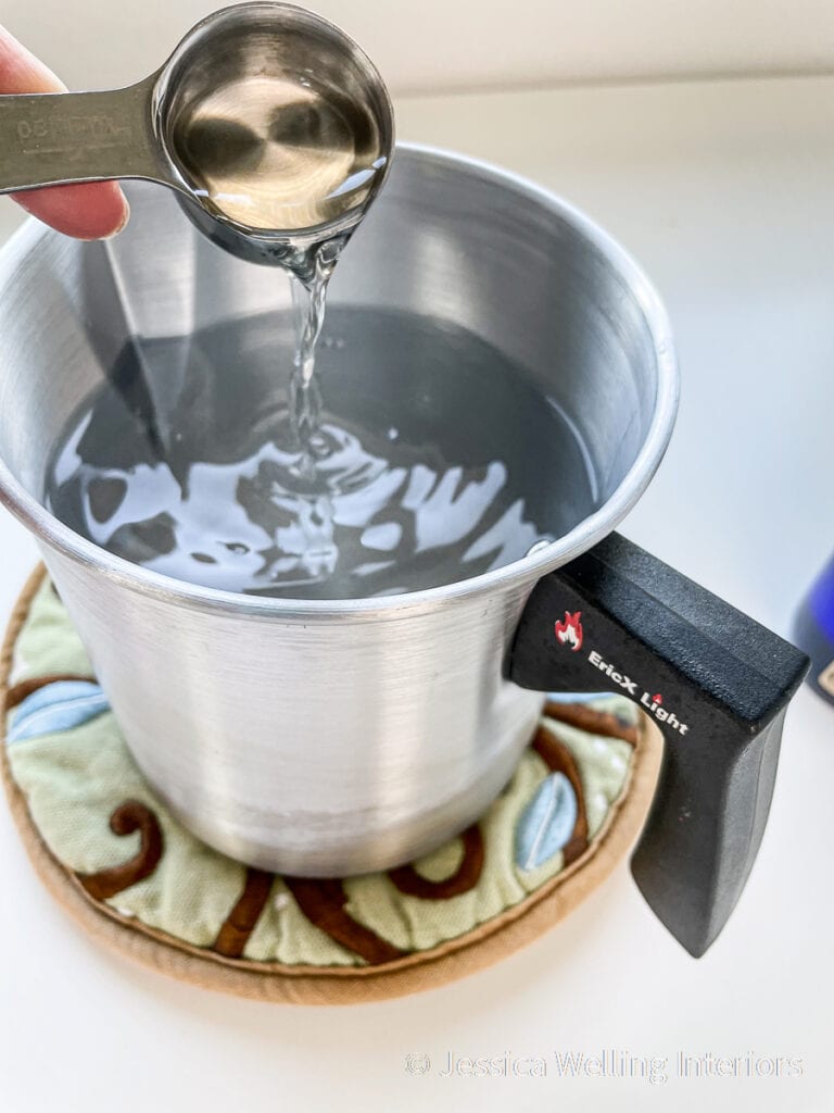 close-up of a measuring spoon pouring citronella oil into a pitcher of hot candle wax