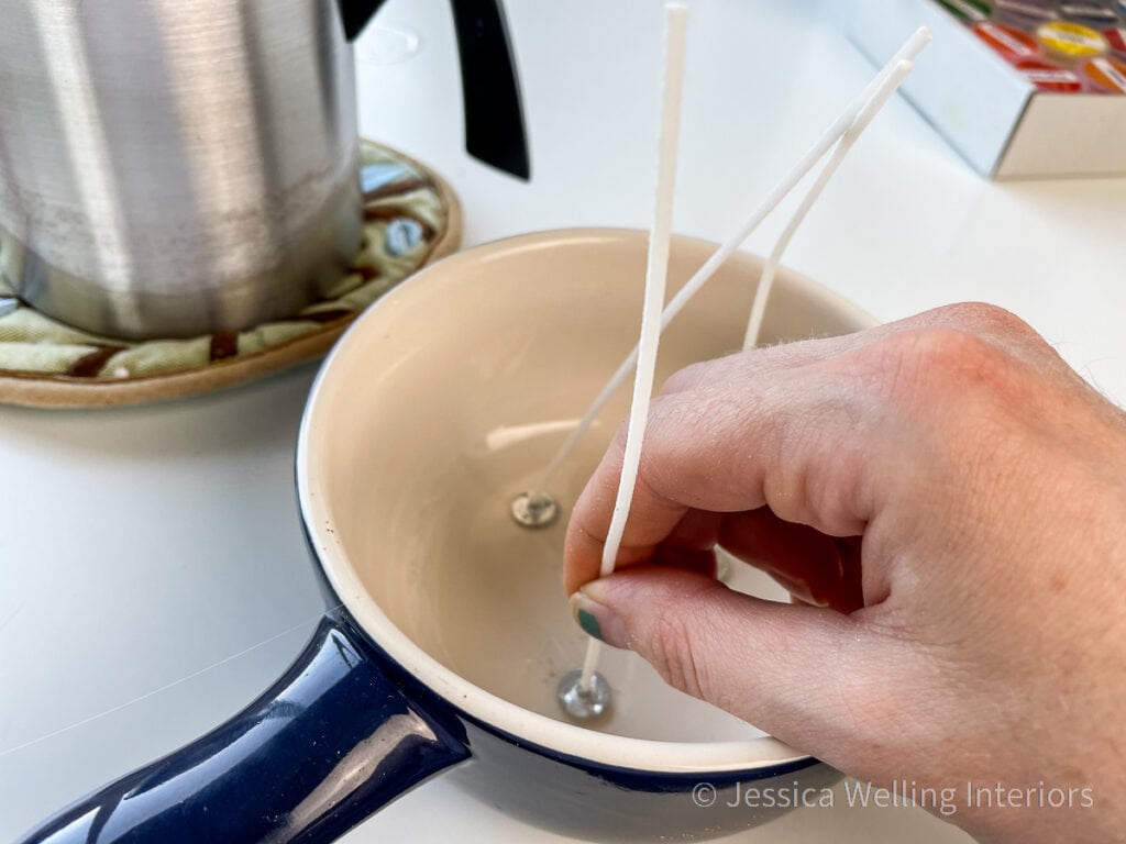 hand attaching 3 candle wicks to the bottom of a ceramic bowl before pouring candle wax