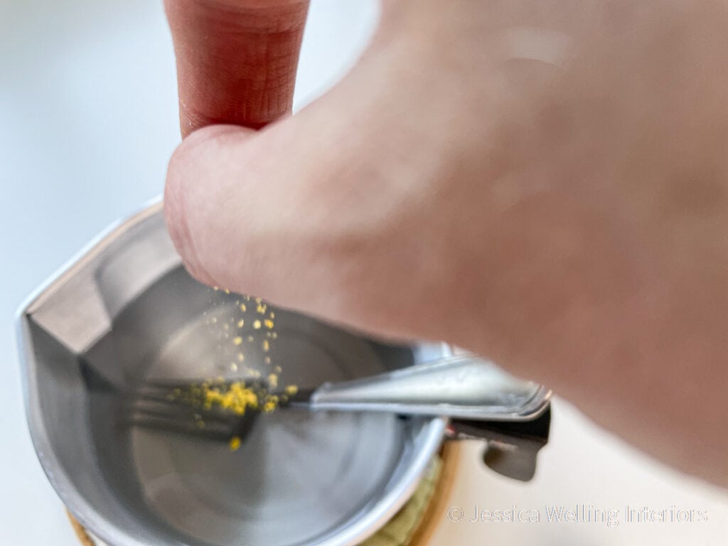 hand sprinking yellow candle dye into melted candle wax